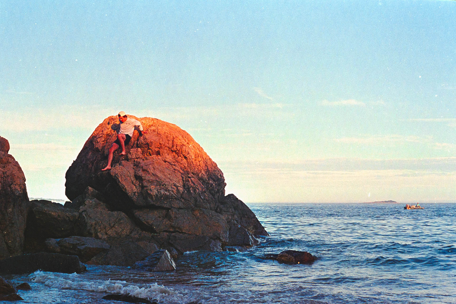Hiker perched on a coastal boulder at sunset